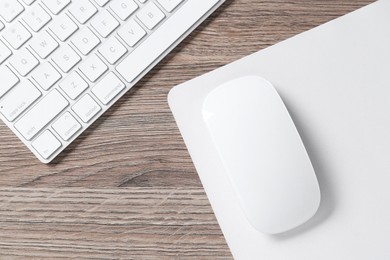 Photo of Computer mouse with mousepad and keyboard on wooden desk, top view