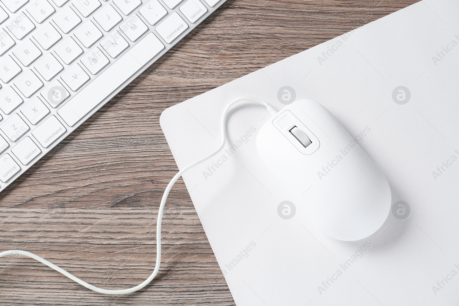 Photo of Computer mouse with mousepad and keyboard on wooden desk, top view