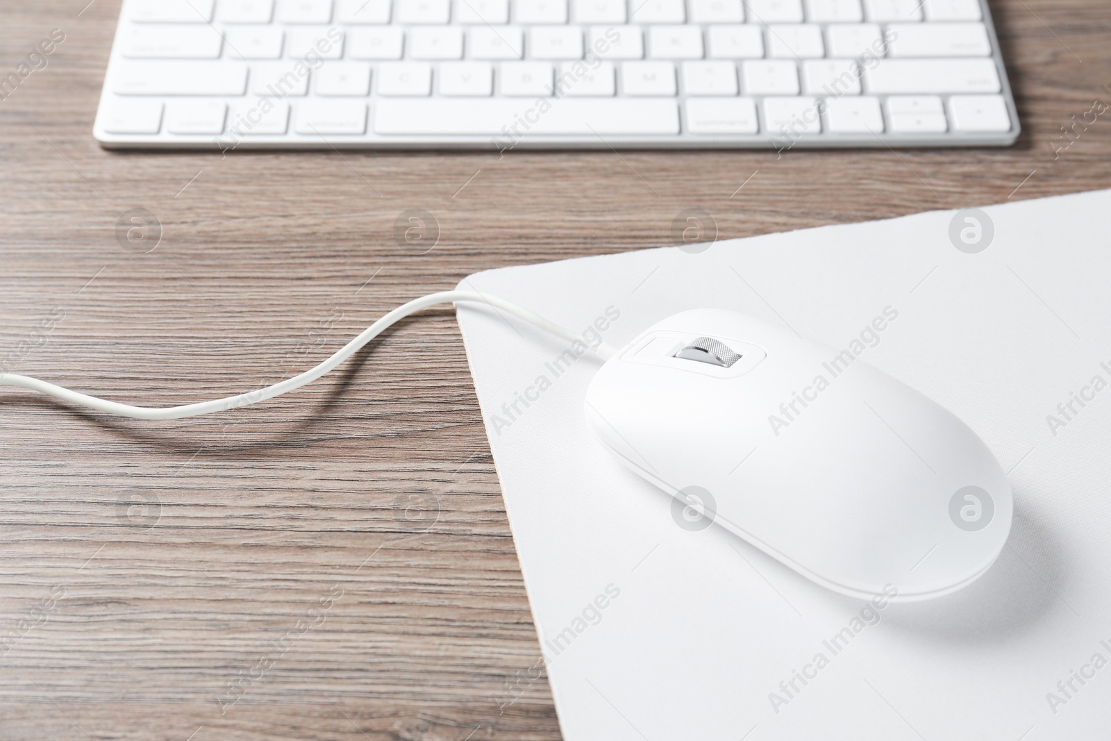 Photo of Computer mouse with mousepad and keyboard on wooden desk, closeup