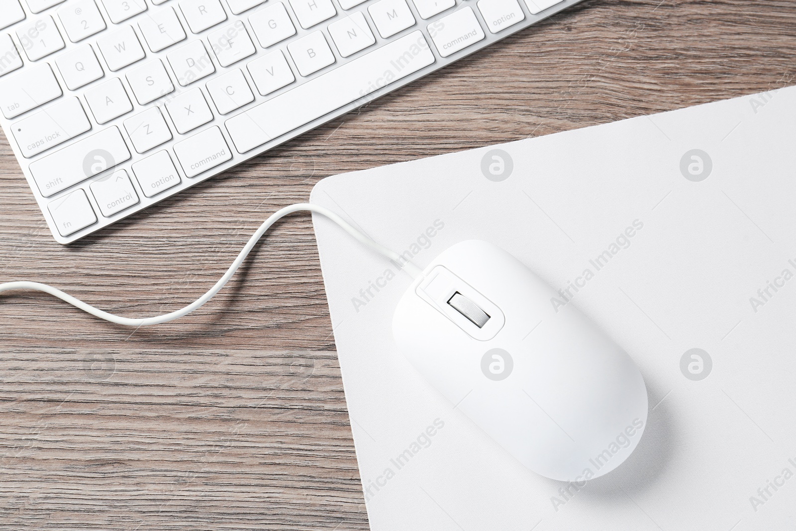 Photo of Computer mouse with mousepad and keyboard on wooden desk, top view