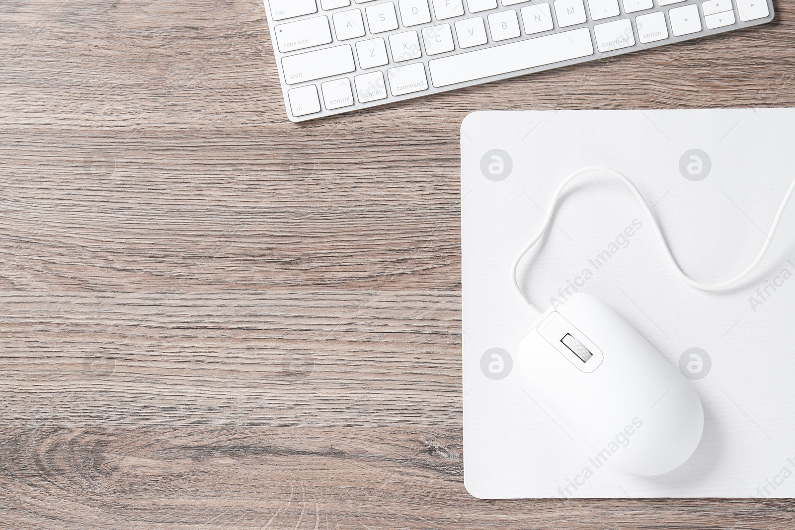 Photo of Computer mouse with mousepad and keyboard on wooden desk, top view. Space for text