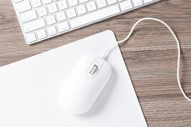 Photo of Computer mouse with mousepad and keyboard on wooden desk, top view