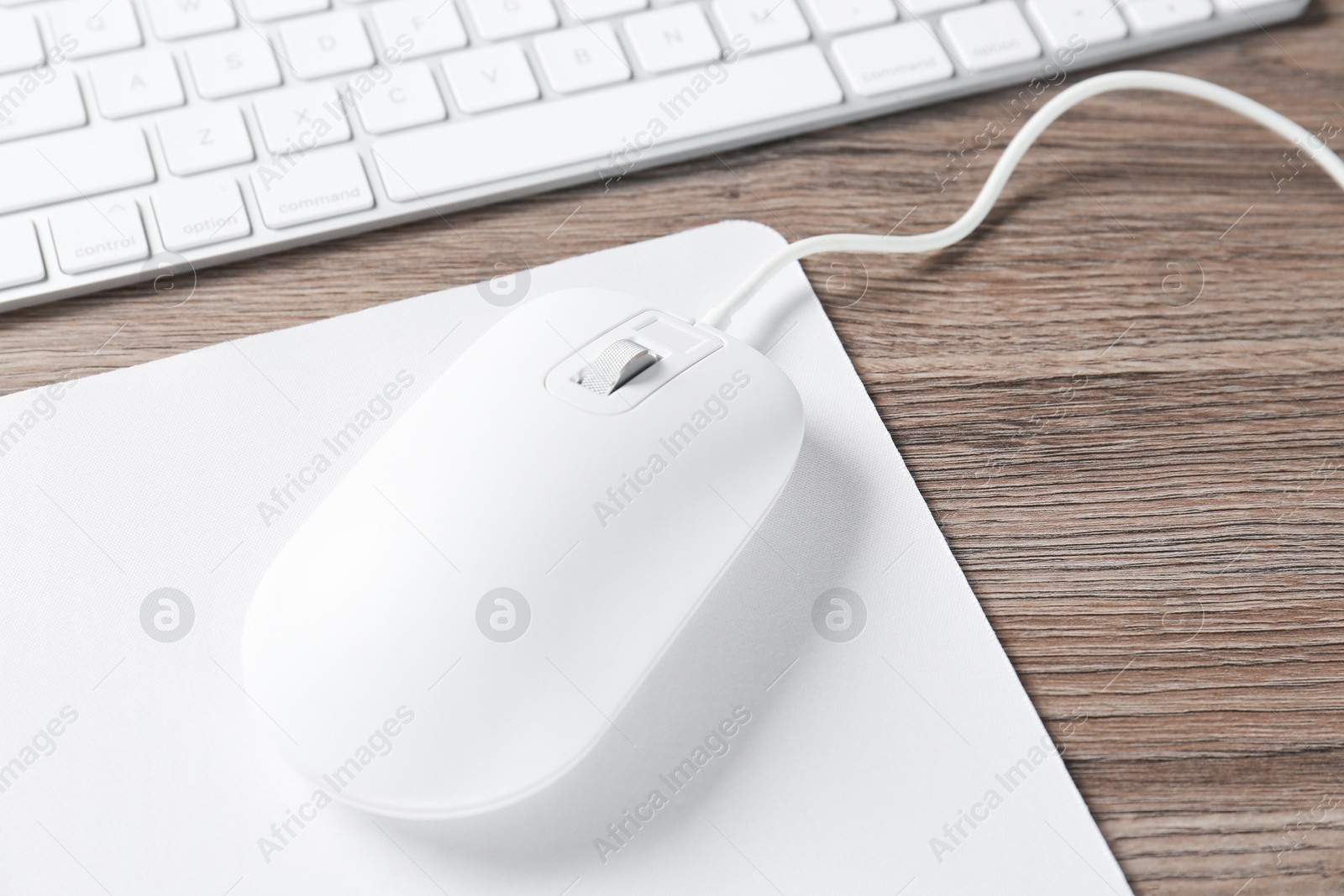 Photo of Computer mouse with mousepad and keyboard on wooden desk, closeup