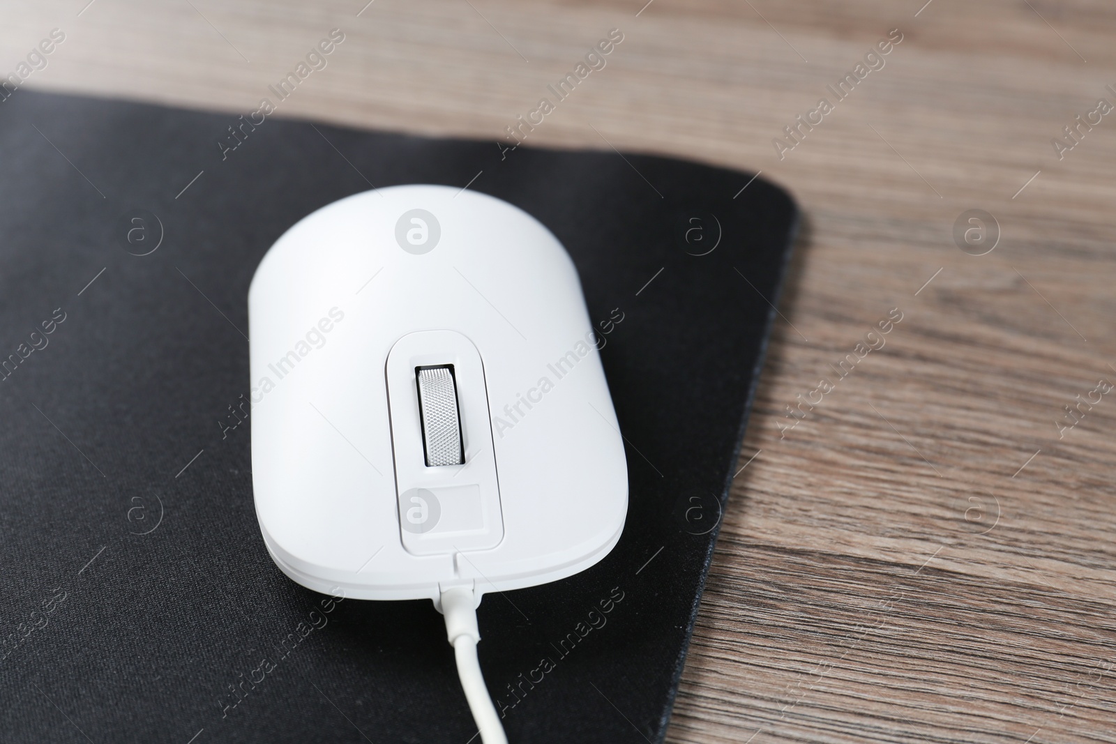 Photo of Computer mouse with mousepad on wooden desk, closeup