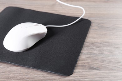 Photo of Computer mouse with mousepad on wooden table, closeup