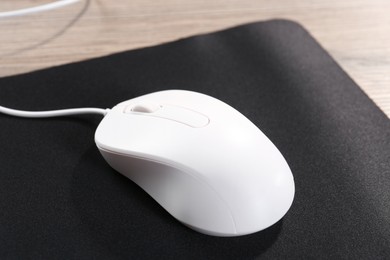 Photo of Computer mouse with mousepad on wooden table, closeup