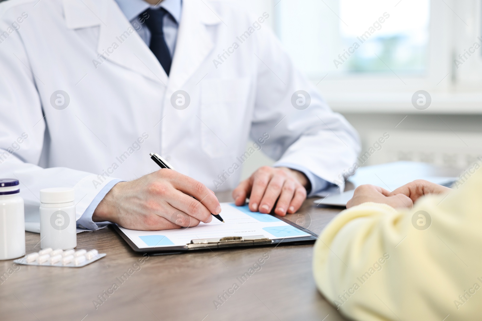 Photo of Doctor writing prescription for patient at wooden table in clinic, closeup