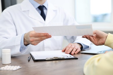 Photo of Doctor giving prescription to patient at wooden table in clinic, closeup