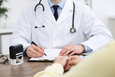 Photo of Doctor giving prescription to patient at wooden table in clinic, closeup