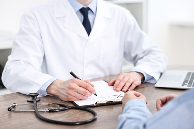 Photo of Doctor writing prescription for patient at wooden table in clinic, closeup