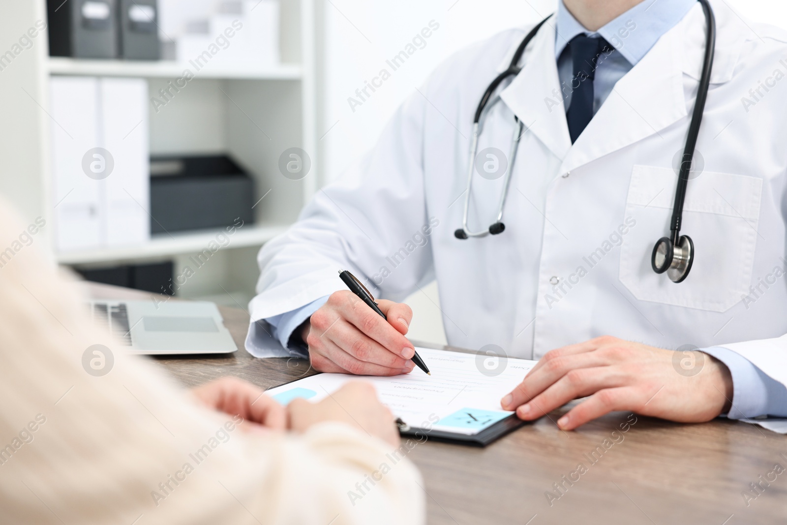 Photo of Doctor writing prescription for patient at wooden table in clinic, closeup