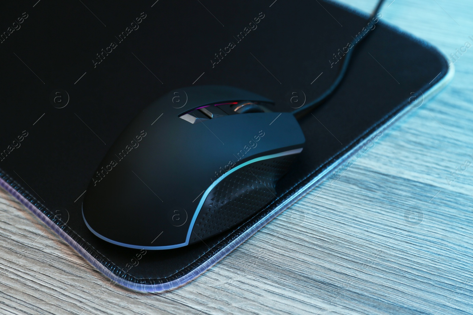 Photo of Computer mouse with mousepad on wooden table, closeup