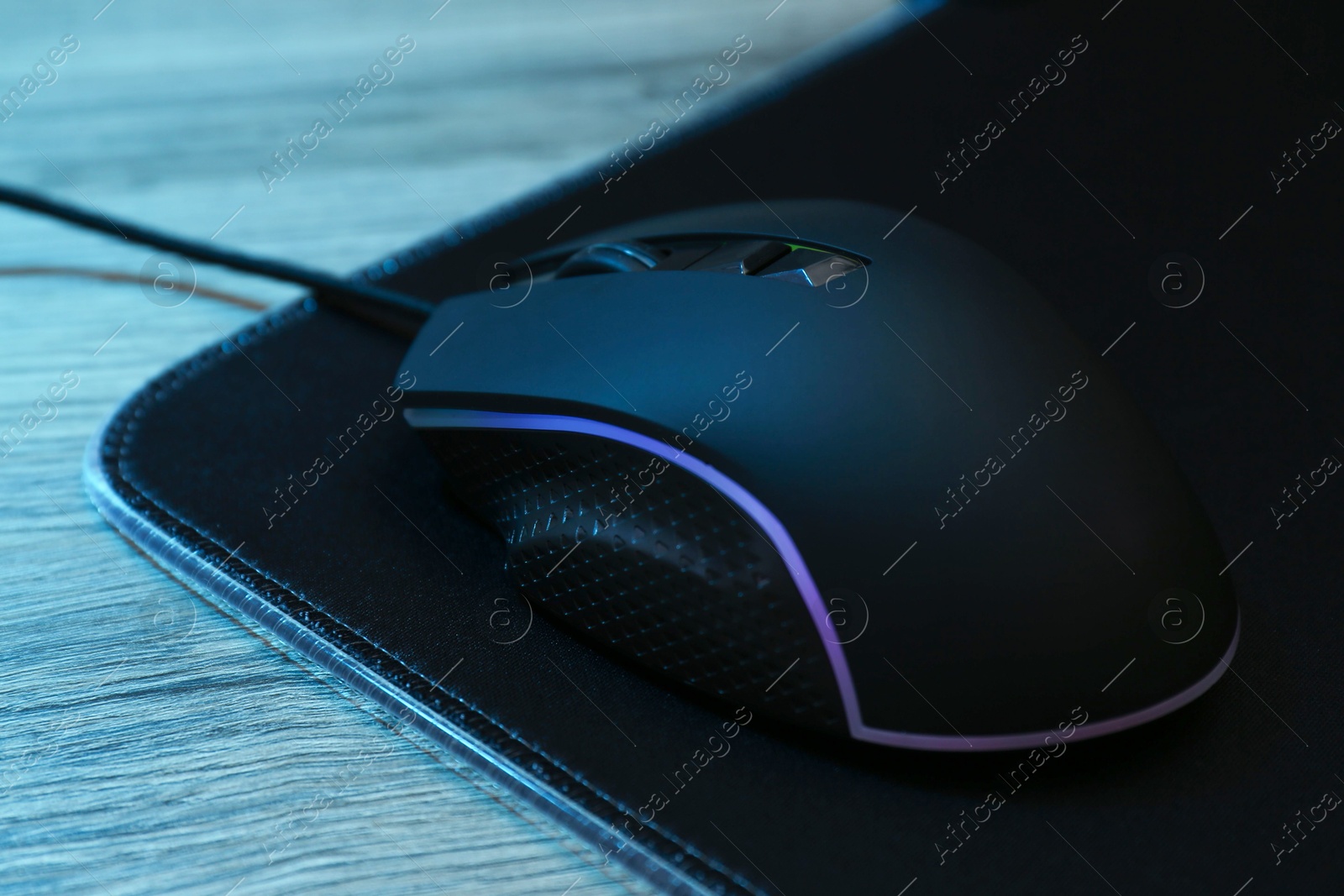 Photo of Computer mouse with mousepad on wooden table, closeup