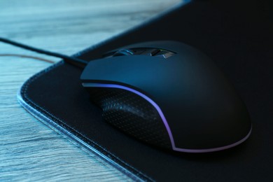 Photo of Computer mouse with mousepad on wooden table, closeup