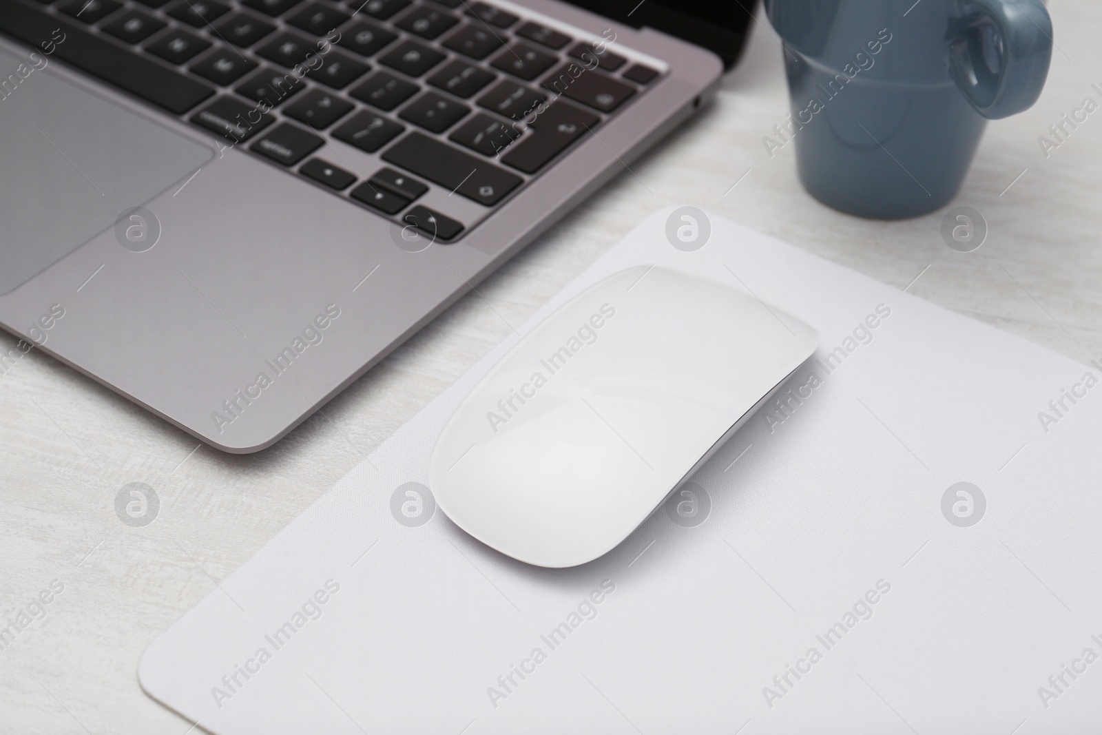 Photo of Computer mouse with mousepad and laptop on light wooden table, closeup