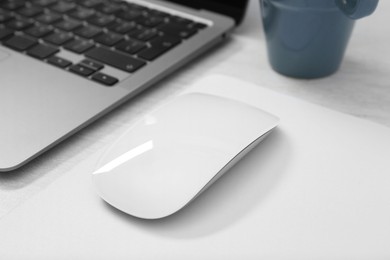 Photo of Computer mouse with mousepad and laptop on light wooden table, closeup