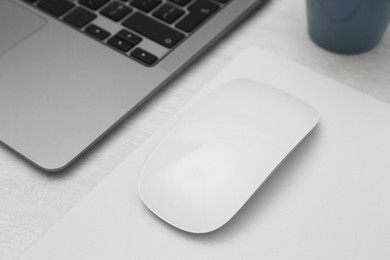 Photo of Computer mouse with mousepad and laptop on light wooden table, closeup