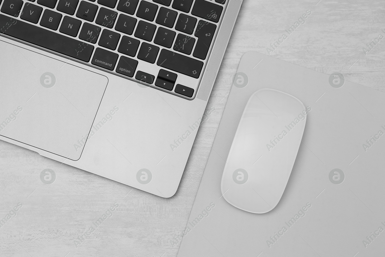 Photo of Computer mouse with mousepad and laptop on light wooden table, flat lay