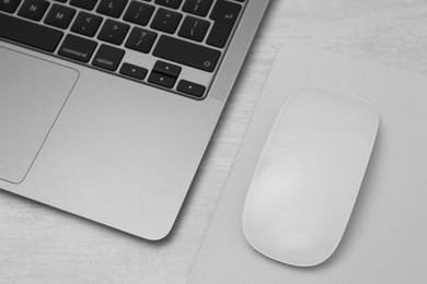 Photo of Computer mouse with mousepad and laptop on light wooden table, closeup