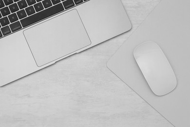 Photo of Computer mouse with mousepad and laptop on light wooden table, flat lay