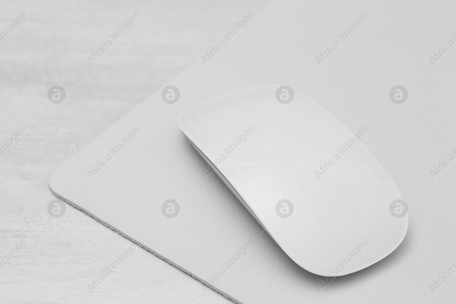 Photo of Computer mouse with mousepad on light wooden table, closeup