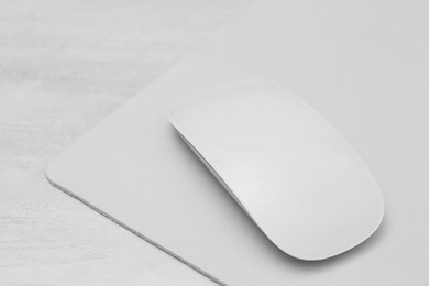 Photo of Computer mouse with mousepad on light wooden table, closeup