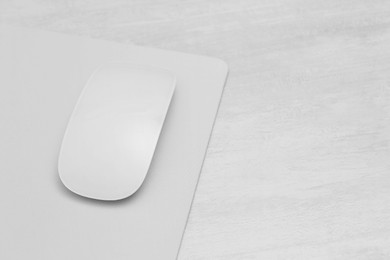 Photo of Computer mouse with mousepad on light wooden table, closeup. Space for text