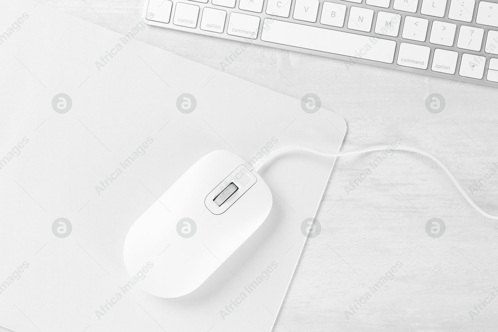 Photo of Computer mouse with mousepad and keyboard on light wooden table, flat lay