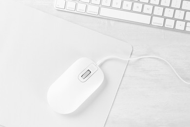 Photo of Computer mouse with mousepad and keyboard on light wooden table, flat lay