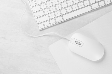 Photo of Computer mouse with mousepad and keyboard on light wooden table, flat lay