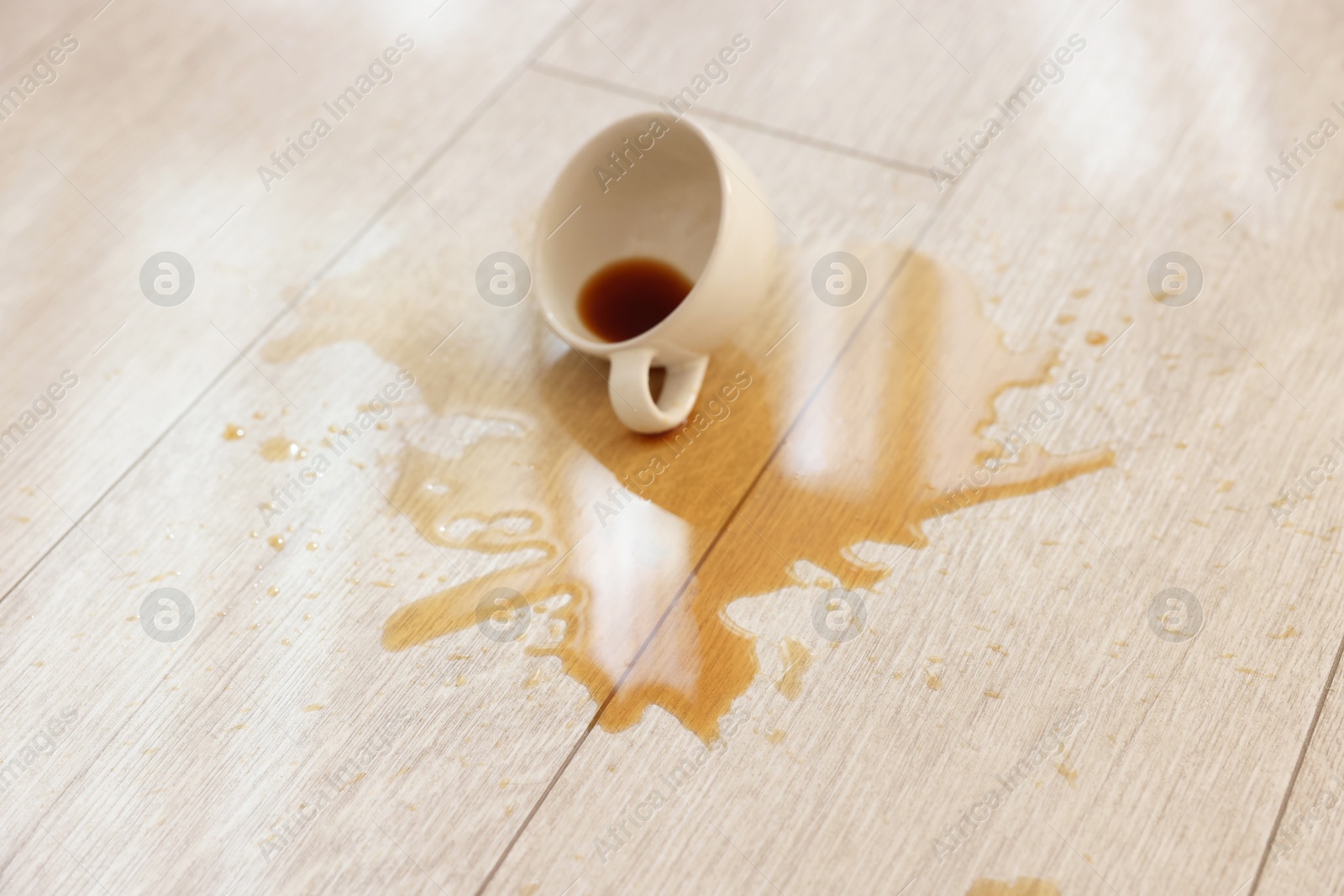 Photo of Cup with spilled drink on wooden floor, closeup