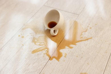 Cup with spilled drink on wooden floor, closeup