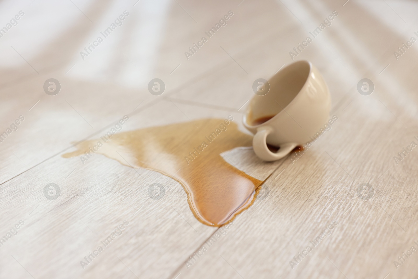 Photo of Cup with spilled drink on wooden floor, closeup