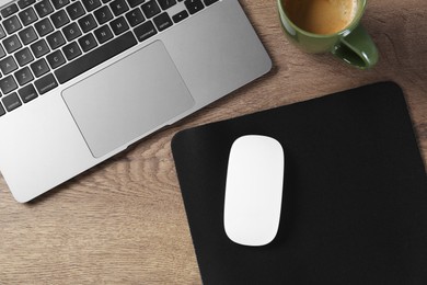 Photo of Computer mouse with mousepad, laptop and cup of coffee on wooden table, flat lay