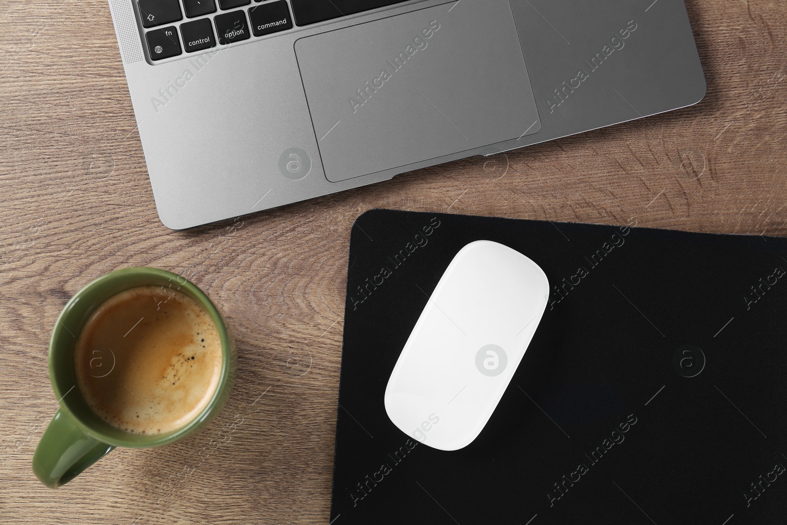 Photo of Computer mouse with mousepad, laptop and cup of coffee on wooden table, flat lay