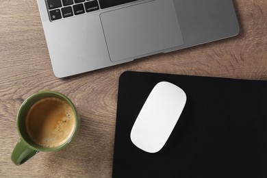 Photo of Computer mouse with mousepad, laptop and cup of coffee on wooden table, flat lay