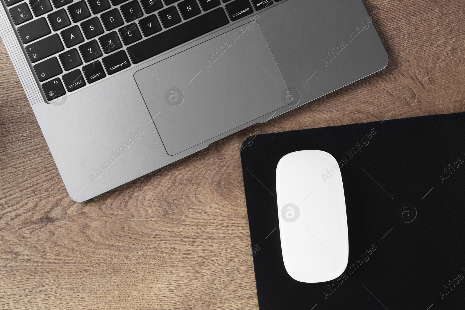 Photo of Computer mouse with mousepad and laptop on wooden table, flat lay