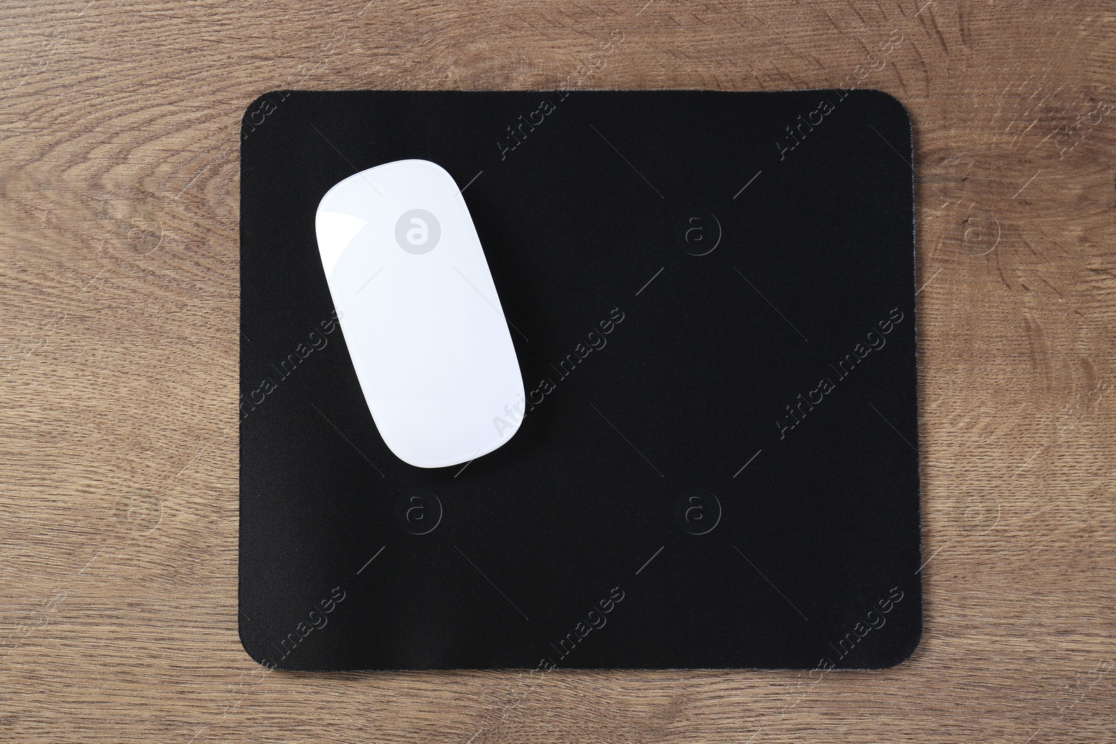 Photo of Computer mouse with mousepad on wooden table, top view