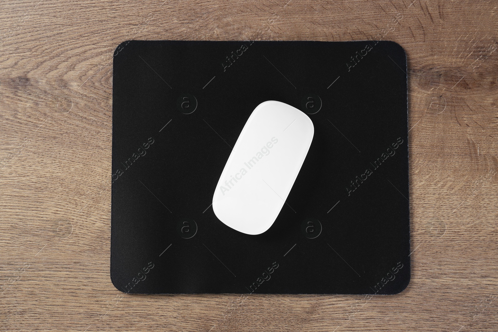 Photo of Computer mouse with mousepad on wooden table, top view