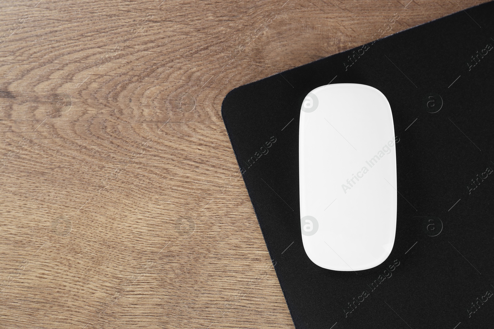 Photo of Computer mouse with mousepad on wooden table, top view. Space for text