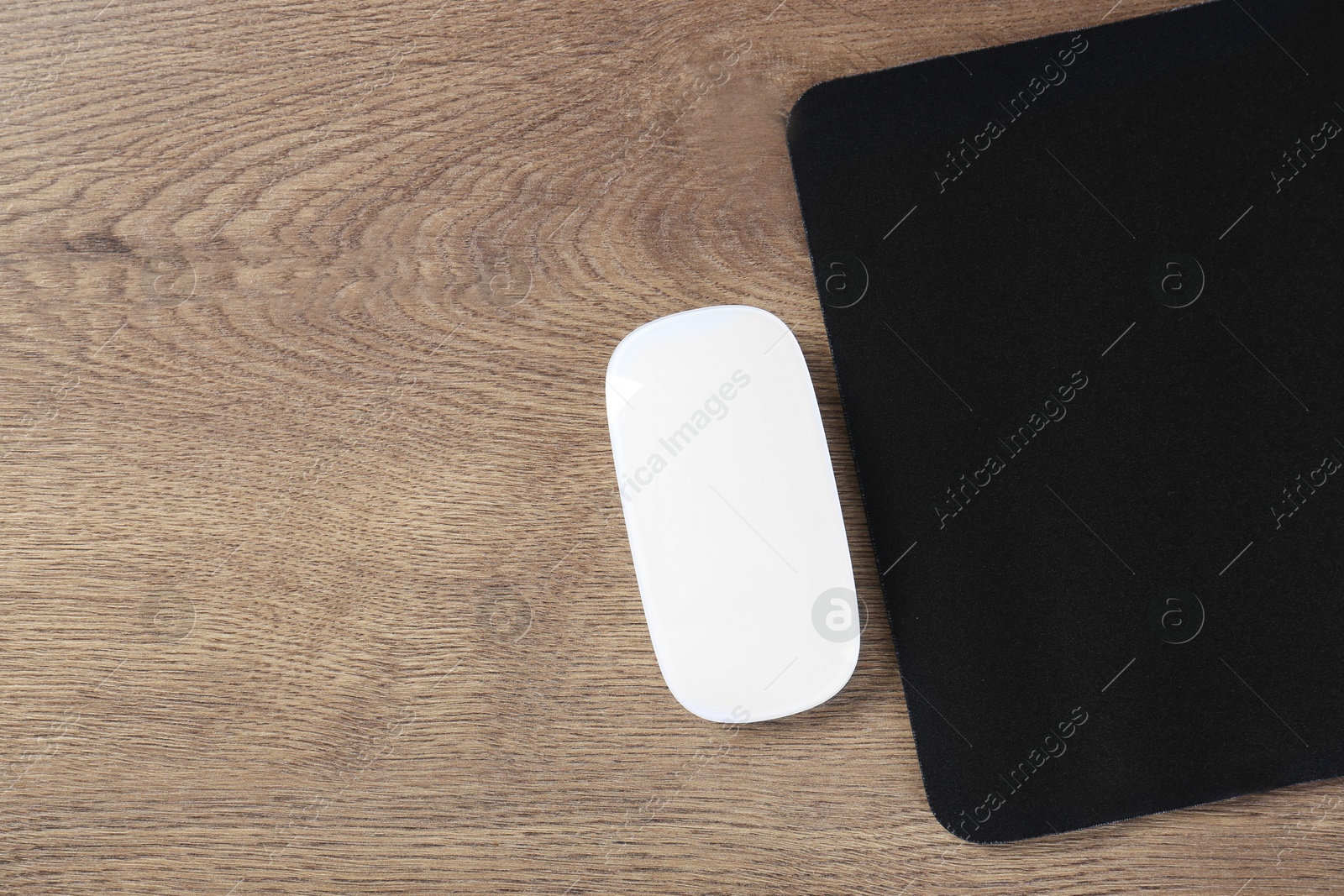 Photo of Computer mouse with mousepad on wooden table, top view. Space for text