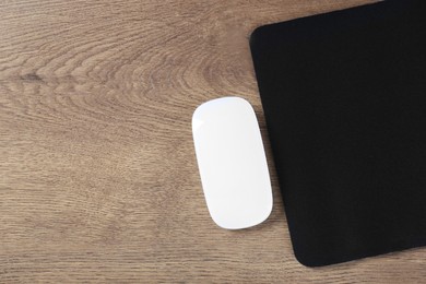 Photo of Computer mouse with mousepad on wooden table, top view. Space for text