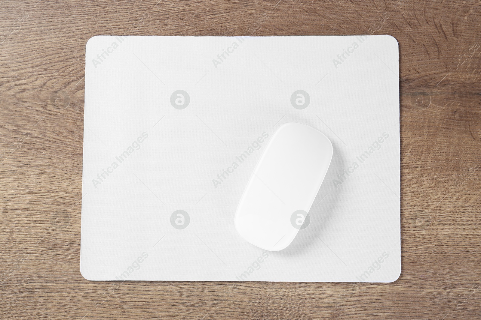 Photo of Computer mouse with mousepad on wooden table, top view