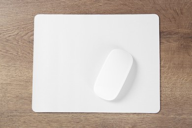 Photo of Computer mouse with mousepad on wooden table, top view