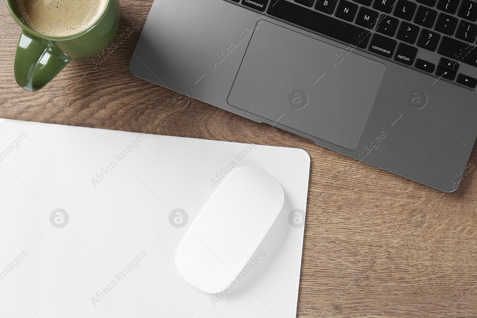 Photo of Computer mouse with mousepad, laptop and cup of coffee on wooden table, flat lay