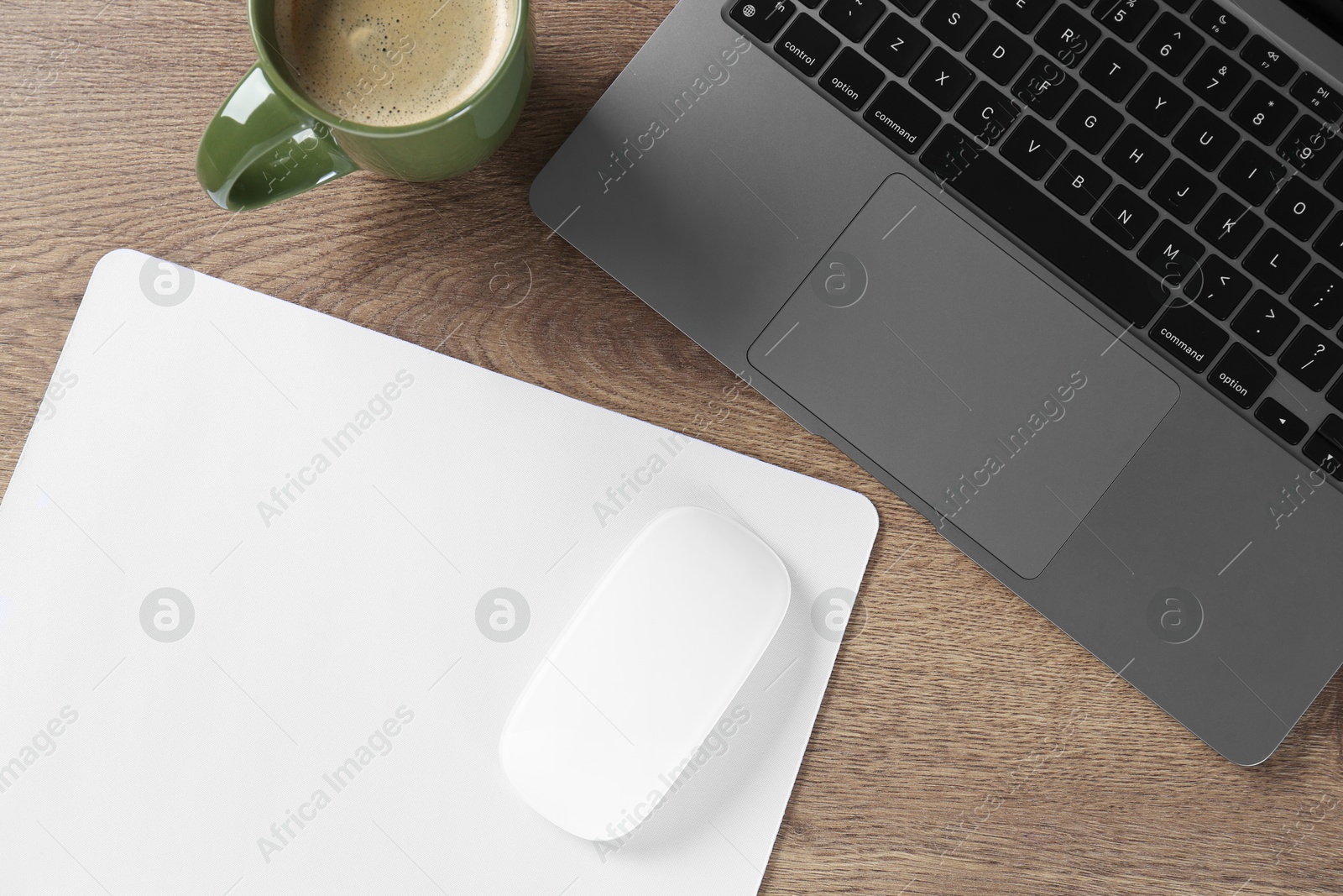 Photo of Computer mouse with mousepad, laptop and cup of coffee on wooden table, flat lay