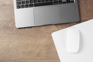 Photo of Computer mouse with mousepad and laptop on wooden table, flat lay