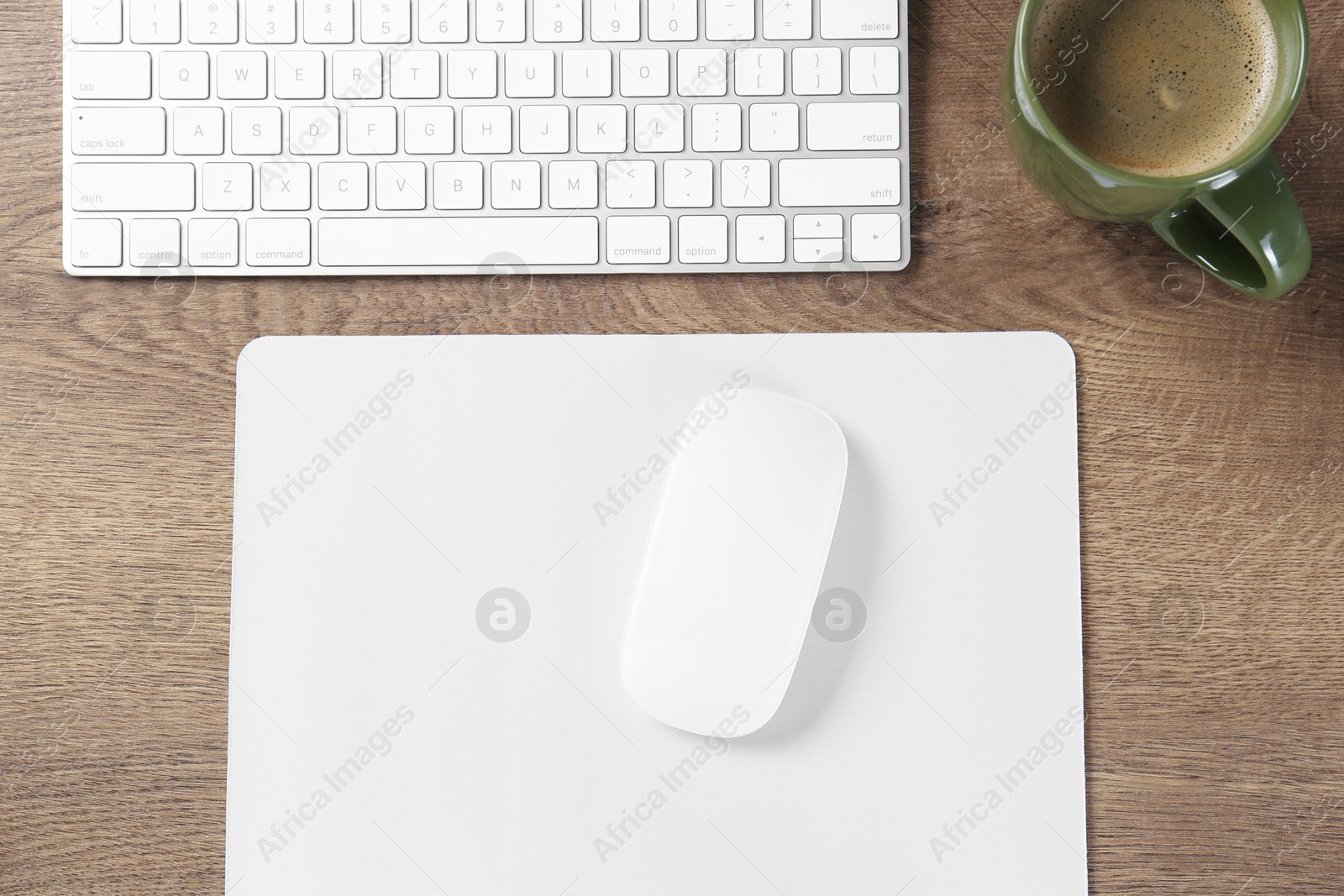 Photo of Computer mouse with mousepad, keyboard and cup of coffee on wooden table, flat lay