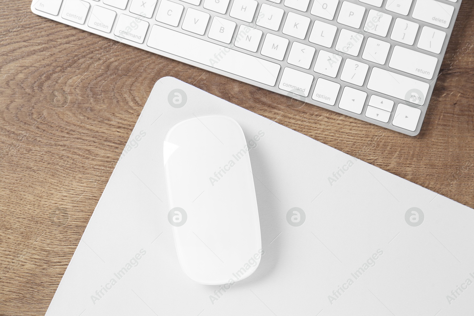 Photo of Computer mouse with mousepad and keyboard on wooden table, flat lay