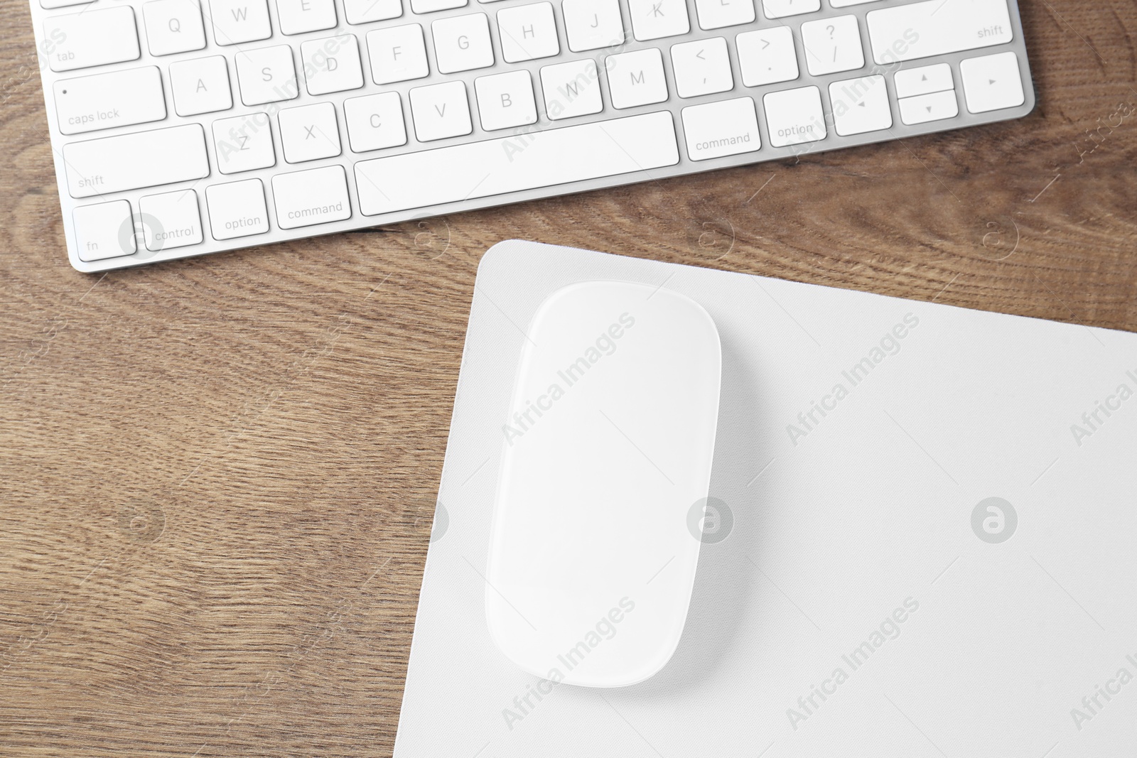 Photo of Computer mouse with mousepad and keyboard on wooden table, flat lay